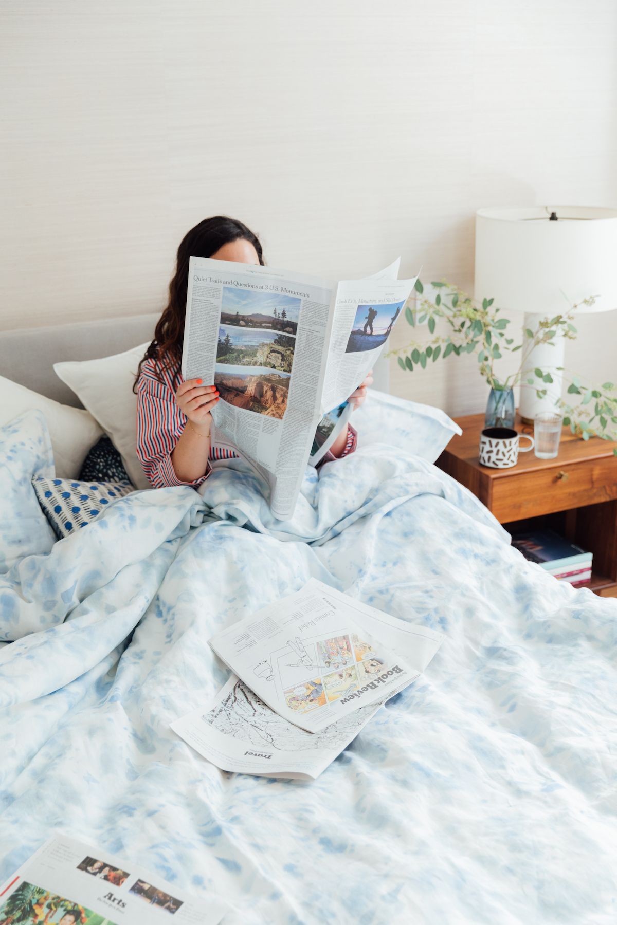 Rebecca Atwood lukee sanomalehteä sängyssä, sinisellä valtameren pussilakanalla