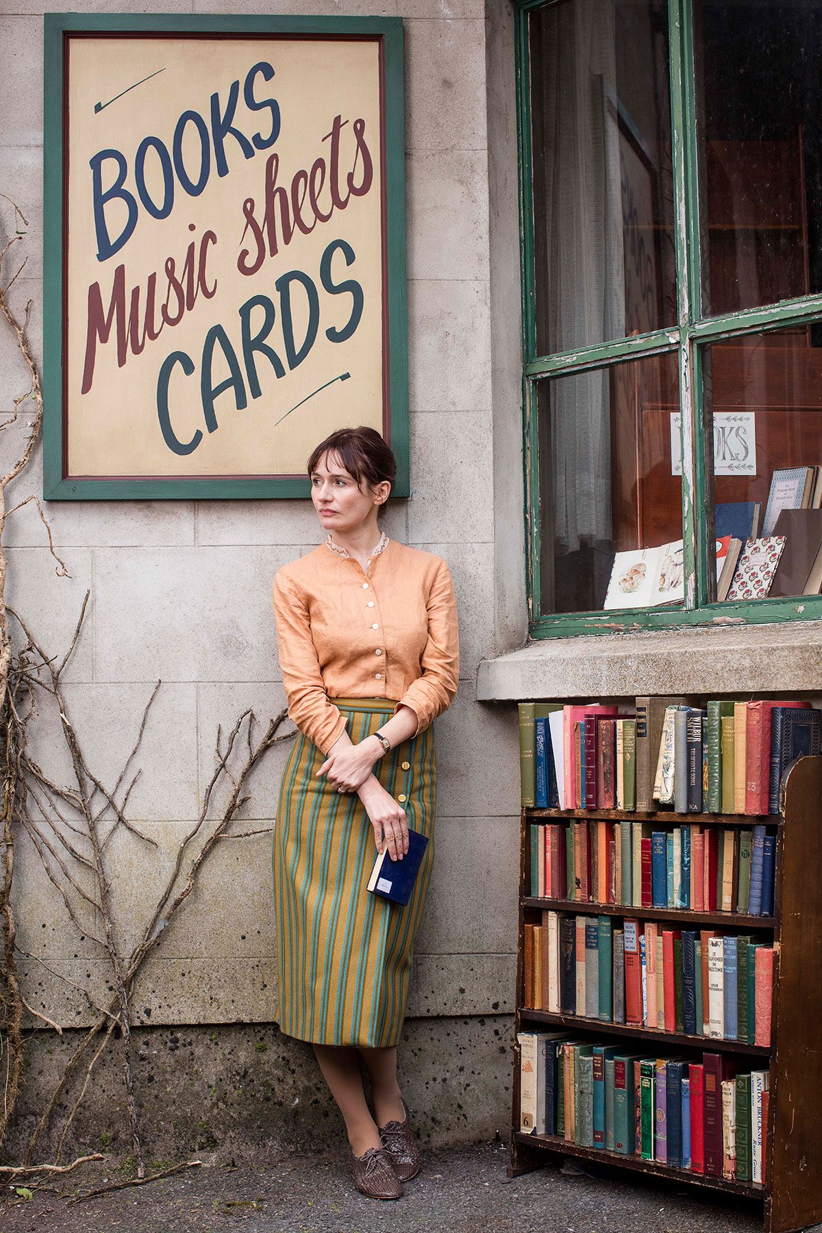 მსახიობი ემილი მორტიმერი წიგნის მაღაზიის გარეთ დგას The Bookshop ფილმში