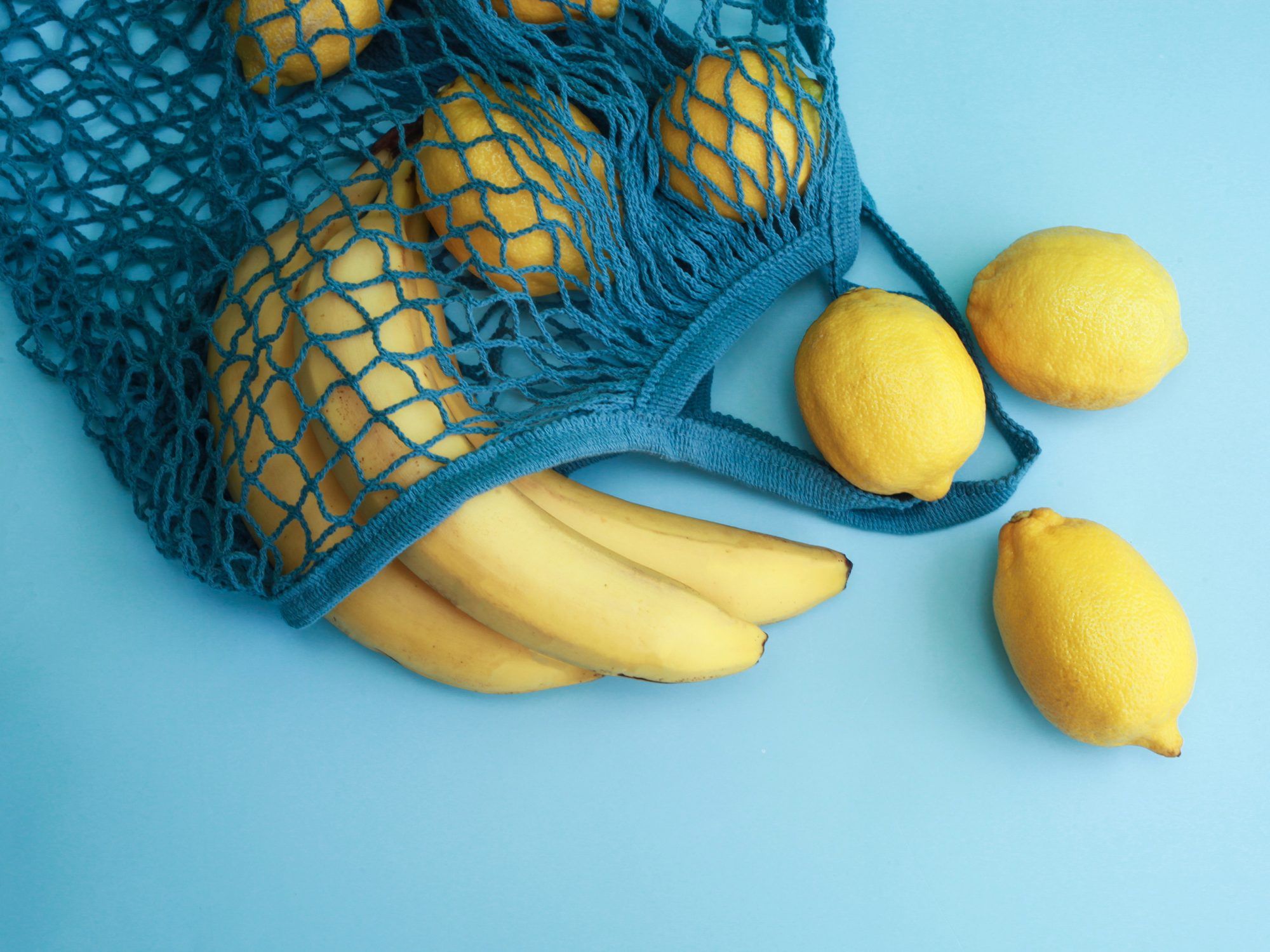 فواكه الليمون الصفراء في كيس شبكي أزرق على خلفية زرقاء مع مساحة نسخ