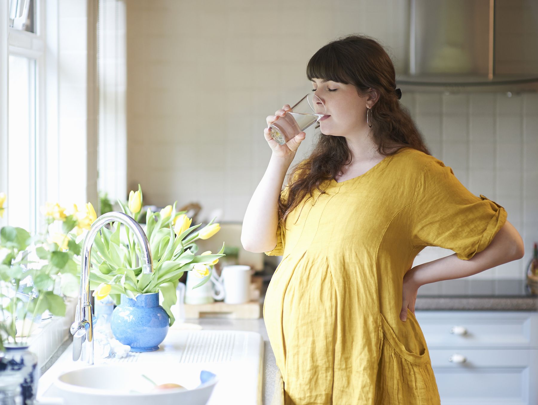 Tehotná žena pije vodu v kuchyni