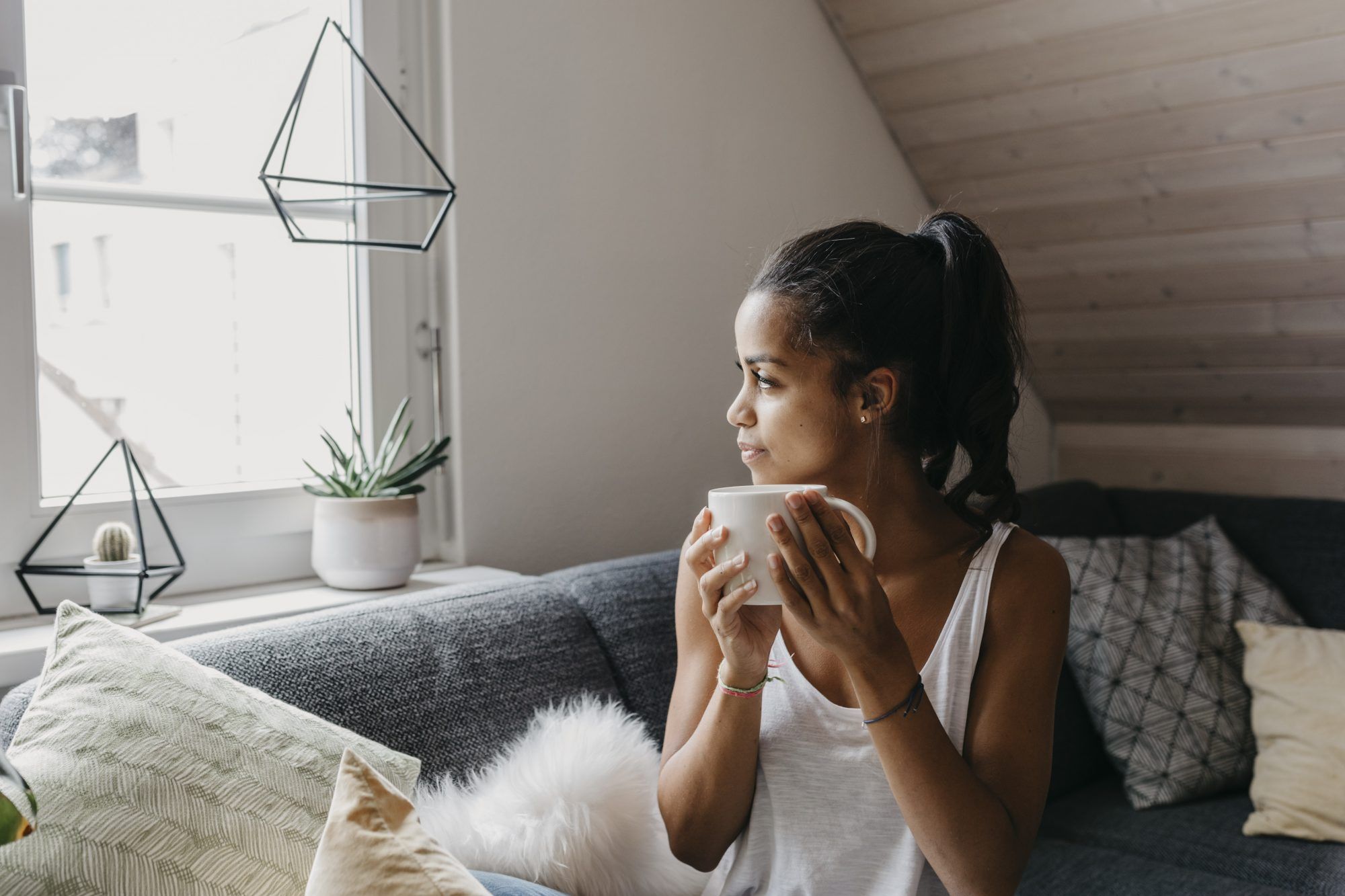 Junge Frau mit Tasse Kaffee auf der Couch sitzend: Morgenroutine