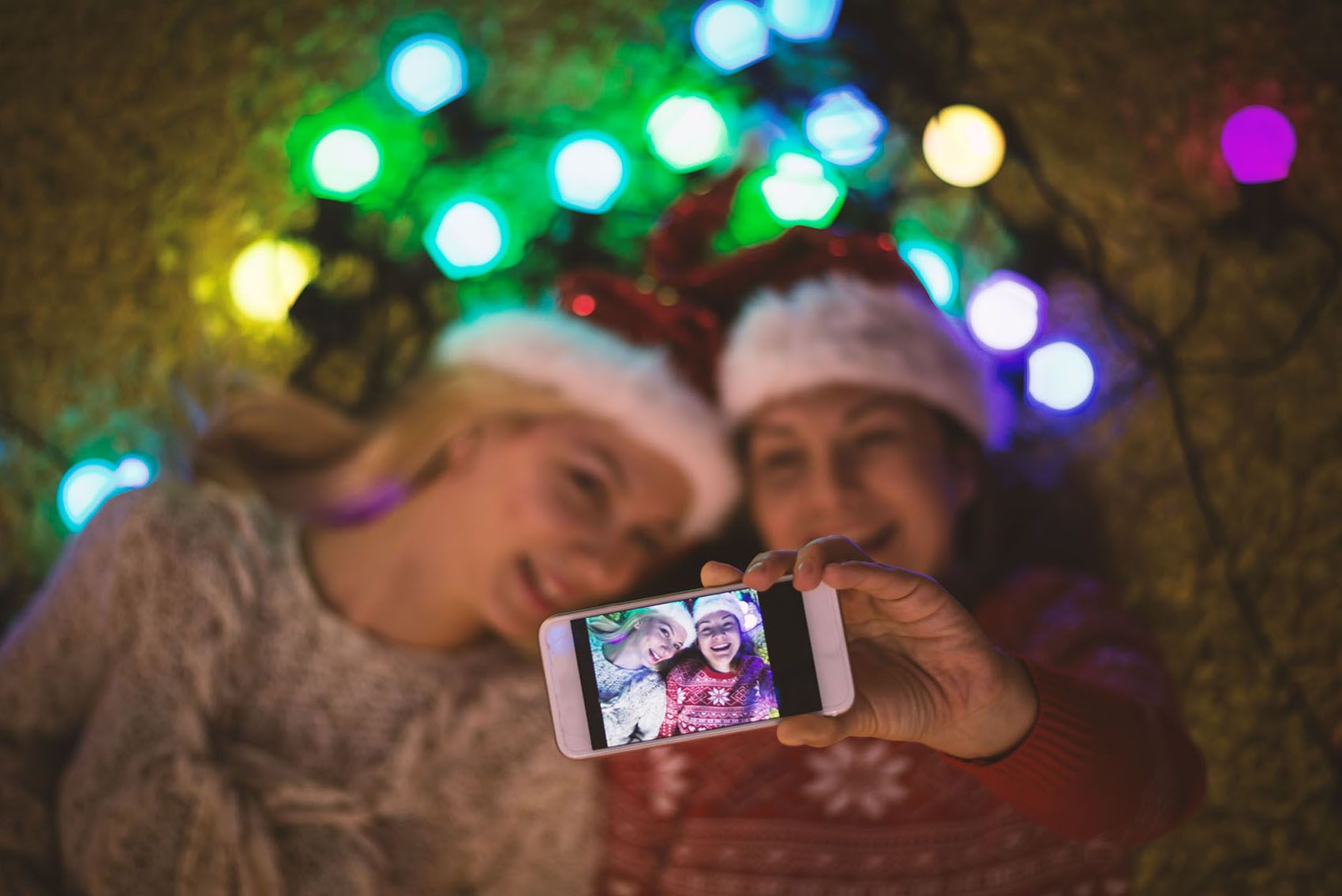 Două fete care își fac selfie-ul de vacanță cu telefonul inteligent împotriva luminilor colorate