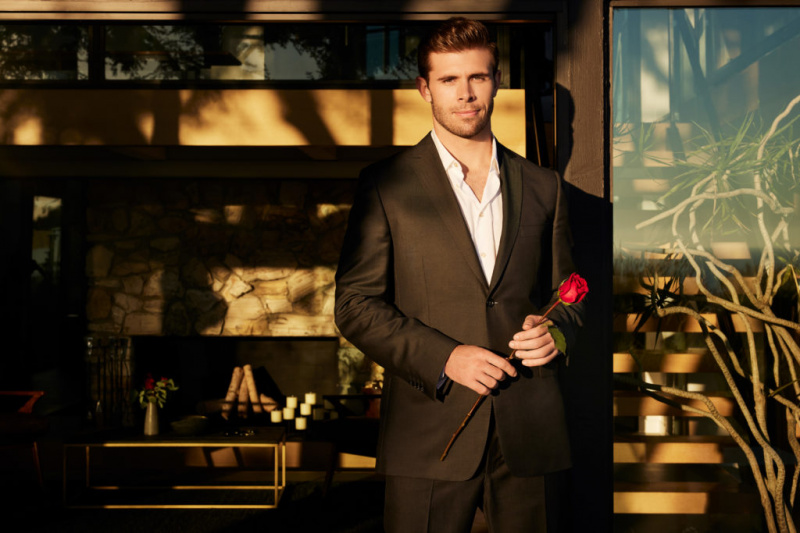   Der Bachelor 2023 Zach Shallcross steht im Anzug und hält eine rote Rose in der Hand