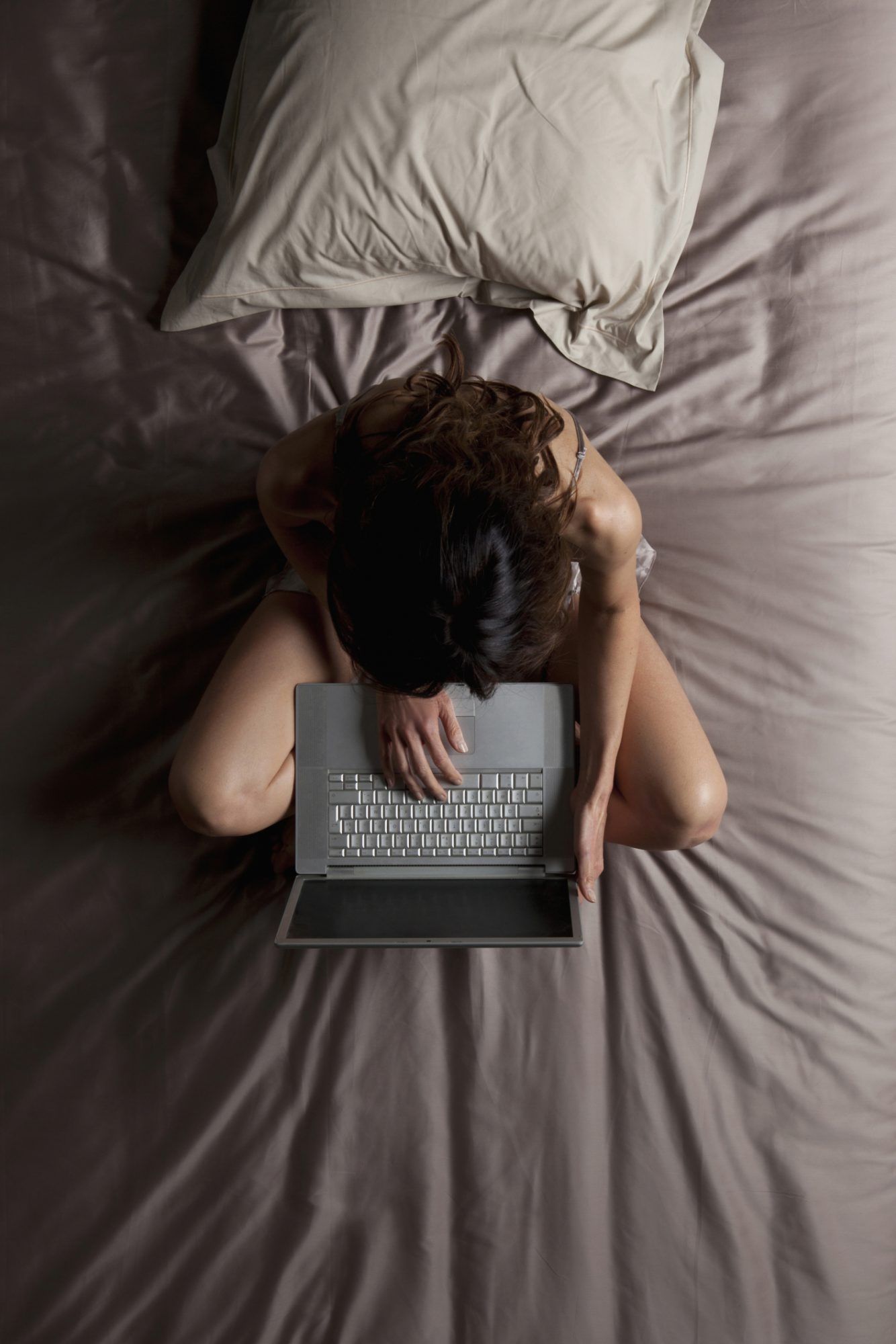 Fotografía cenital de una mujer sentada en la cama escribiendo en la computadora