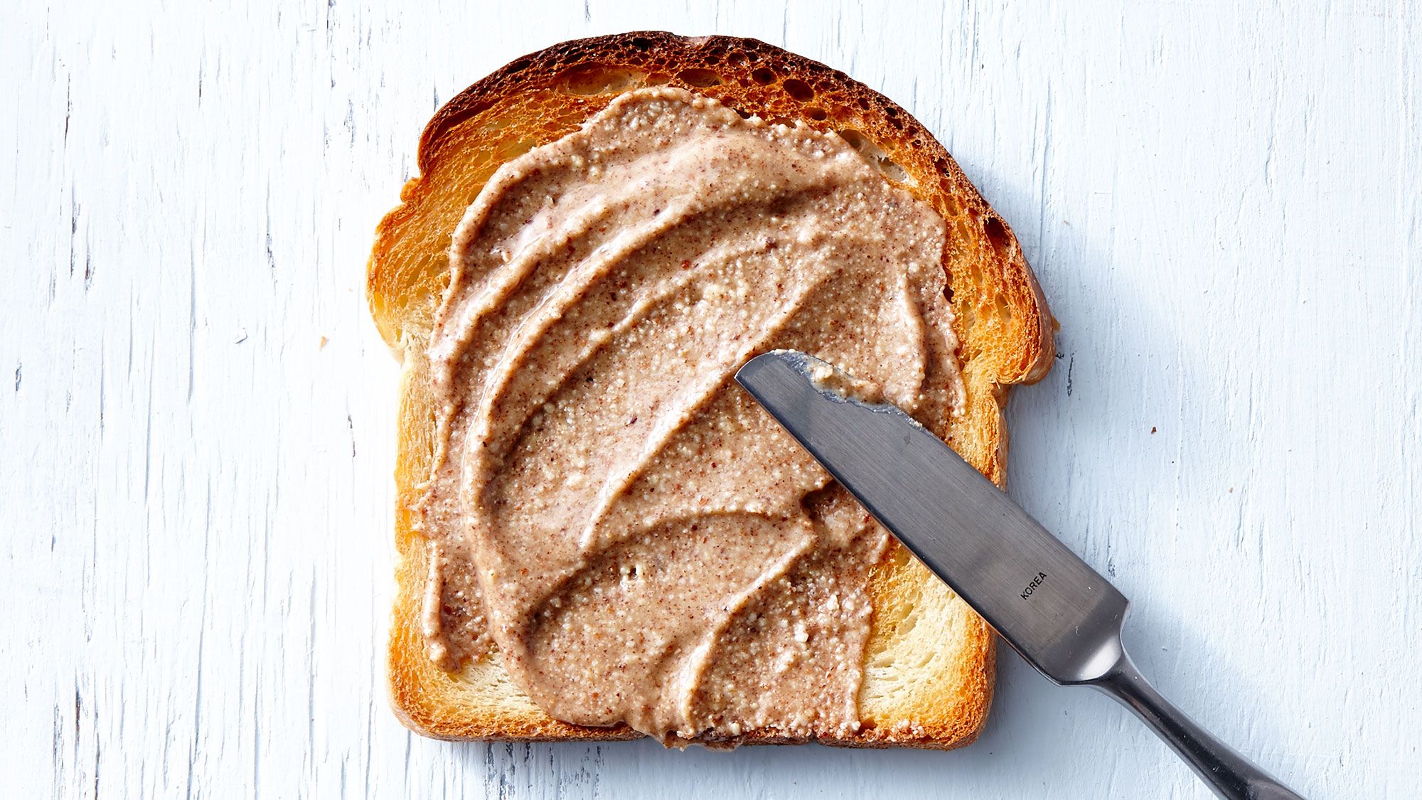 Лучшие ореховые масла: нож, намазывающий ореховое масло на хлеб