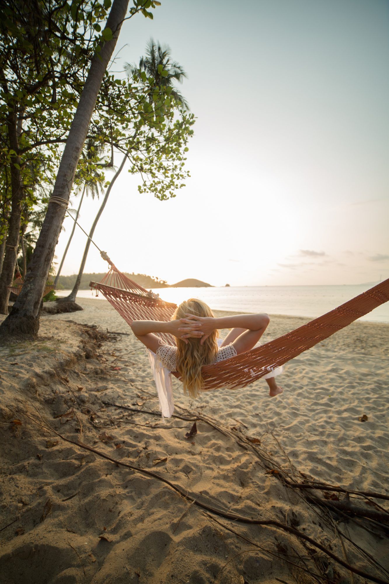 Ženska na tropski plaži, ki leži na viseči mreži